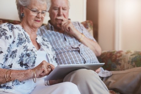Elderly couple sat on a sofa looking at a tablet device together